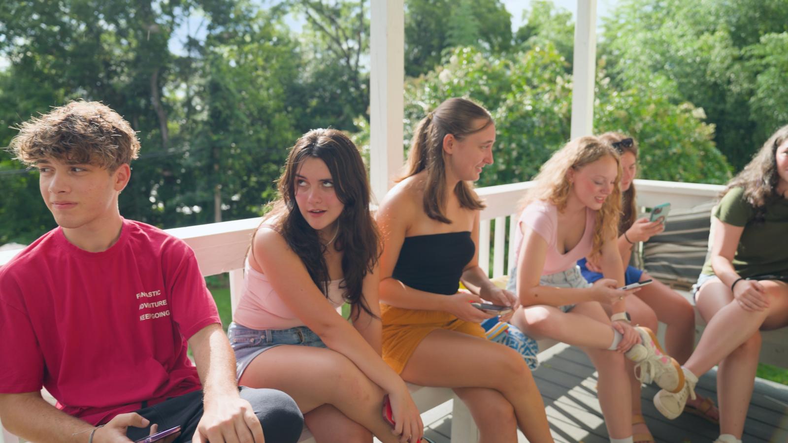 Teen a cappella singers on a porch, one rolling her eyes