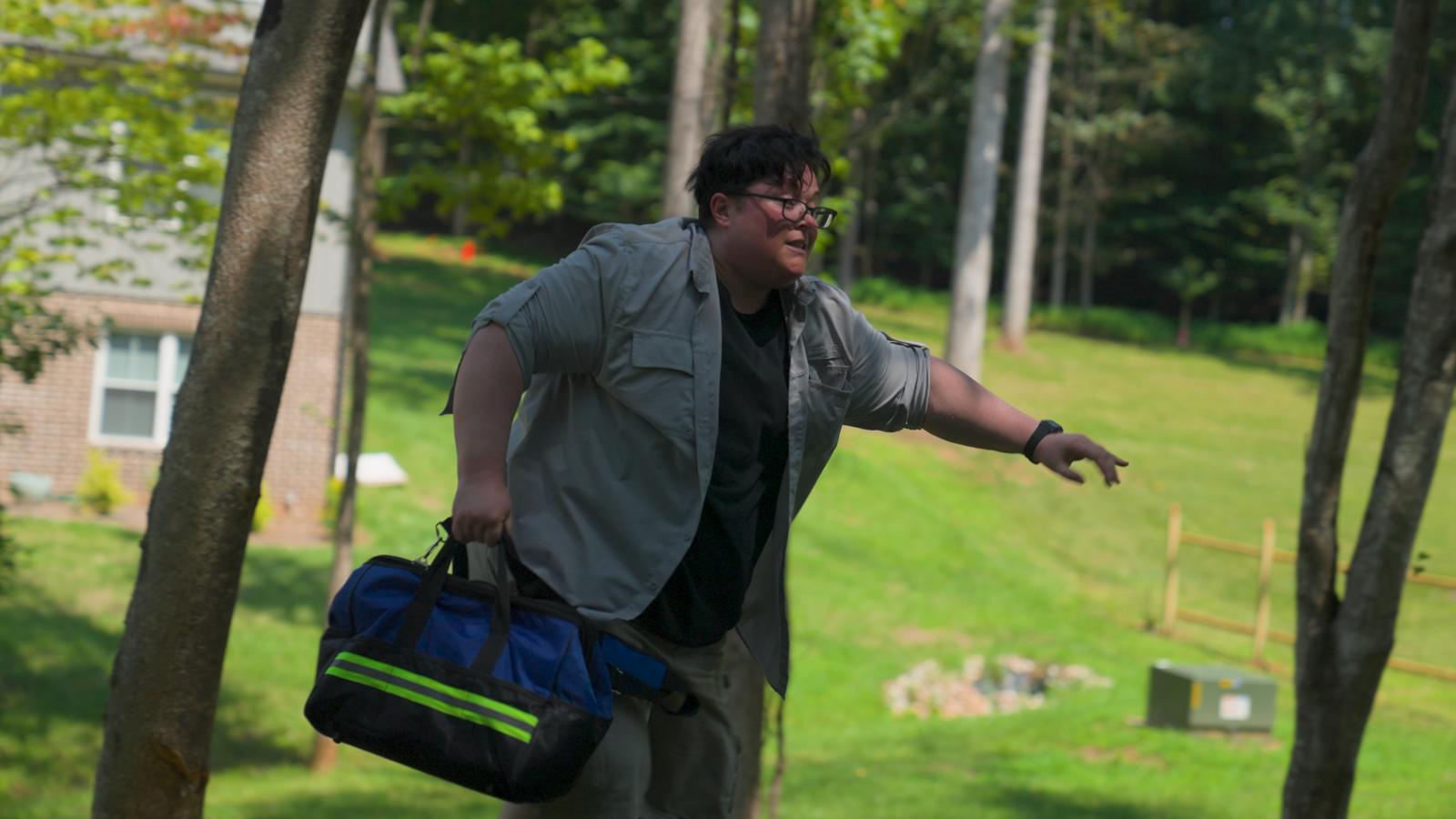 Denni flees across a yard with a duffel bag