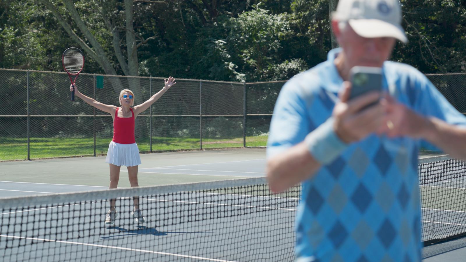 Lucy celebrates on the tennis court while Wayne checks his phone