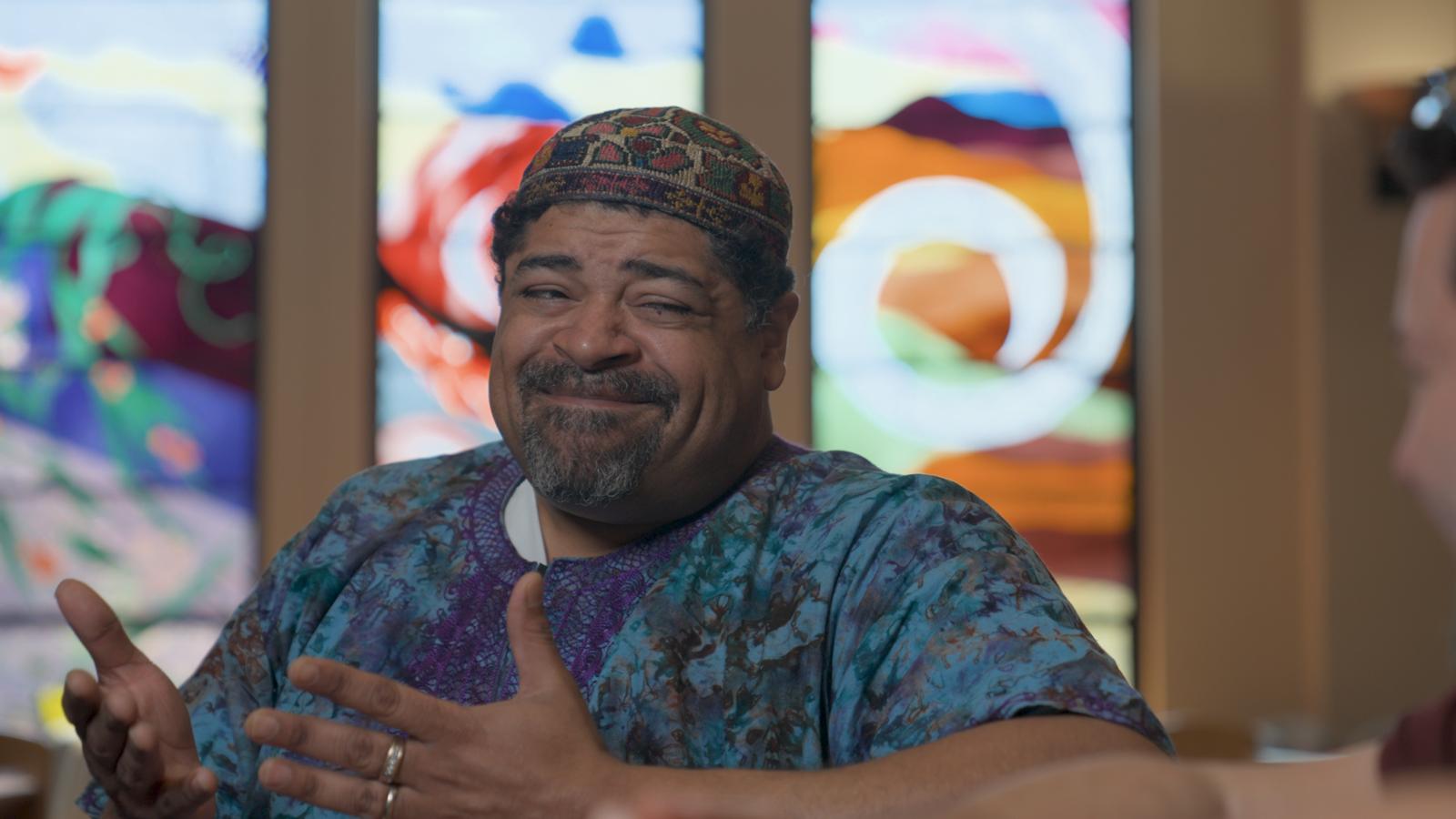 The Rabbi, smiling apologetically in front of stained glass
