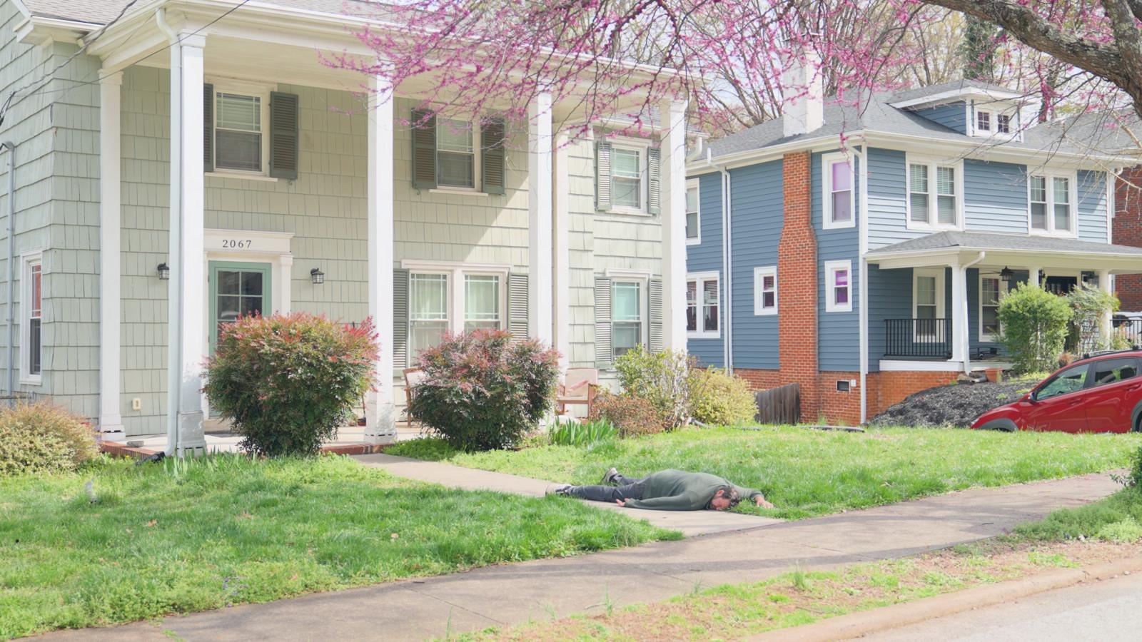 A figure lies on a front lawn