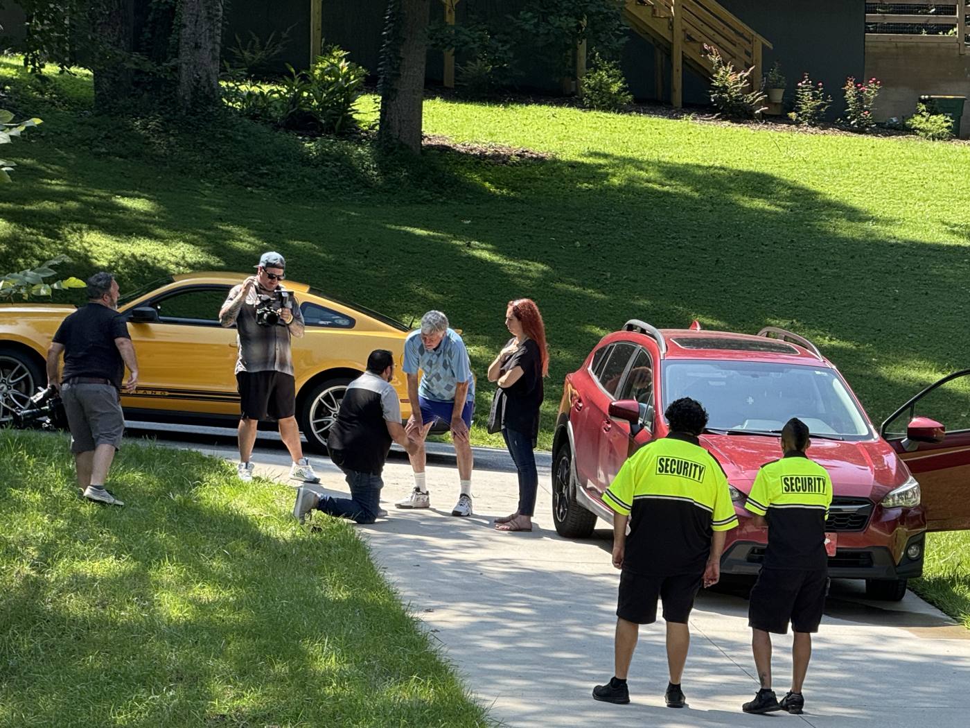 Brad kneels by Wayne in a driveway as the crew films